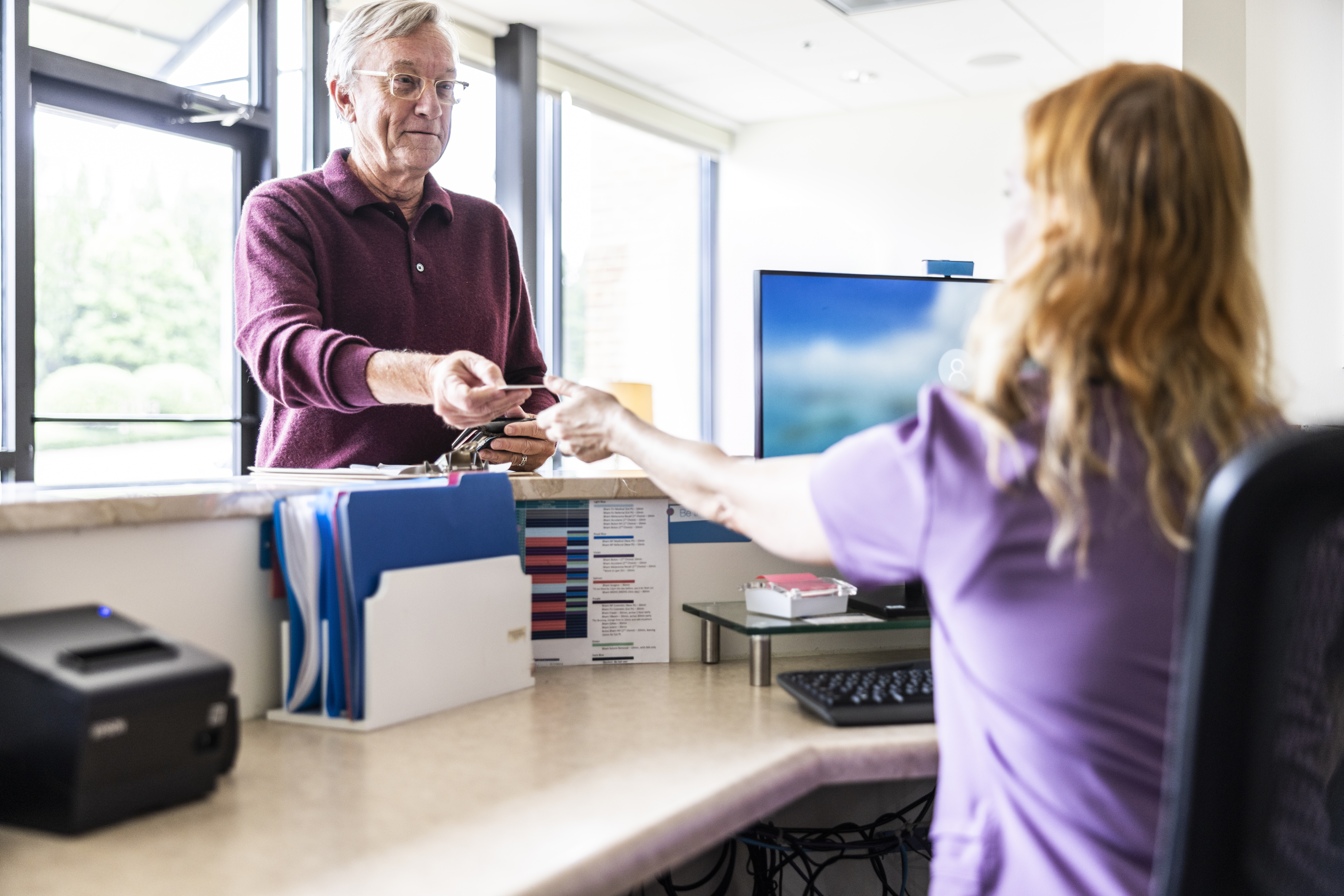 Senior man paying with credit card at doctor's office front desk